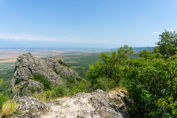 View of the Alazani Valley from a high mountain. Rocks and trees around. Agrarian fields are...