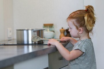 Little girl in a kitchen with a saucepan on hob with a wooden spoon