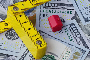 A centimeter ruler and a model house displayed against a background of one hundred dollar bills, illustrating the concept of fluctuating apartment and house prices depending on market rates and credit