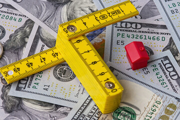 A centimeter ruler and a model house displayed against a background of one hundred dollar bills,...