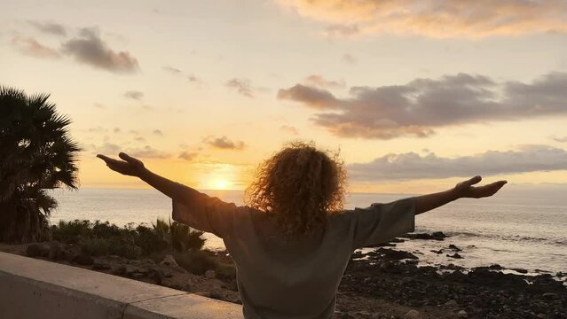 One happy woman tourist with curly hair admiring enjoying sunset on the ocean. People and wellbeing with nature and vacation outdoor leisure activity in front of a golden sunrise on the sea surface.