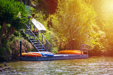 Colourful kayaks drying on a private jetty hidden in the lush green at the bottom of a steep hill