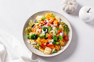 Autumn pasta salad with roasted pumpkin, broccoli, feta cheese on bright light background, fall season salad