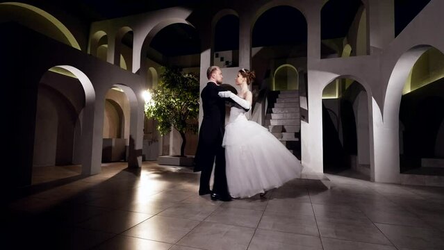 happy loving couple in gorgeous gowns dancing in royal palace in ballroom in night, slow motion shot
