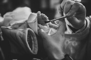 Anointing. Unction at baptism. Priest and godfather stretch hands to legs. Temple, Orthodoxy. Closeup of tiny baby feet, the sacrament of baptism ceremony. Godmother holds child. Black and white photo