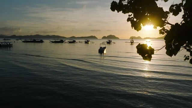 Group of boats in Corong Corong Beach with sunset view through leaves. El Nido, Palawan. Philippines.