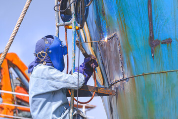 Welder rappelling with ladder to welding metal hull of the old vessel in shipyard area, improvement...