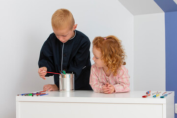 Two young children a girl and a boy having fun with paintbrushes