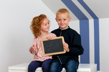 Two young children a girl and a boy smiling holding a wooden black slate