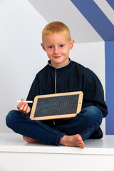 Little blond boy sitting with a chalk slate