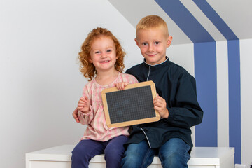 Two young children a girl and a boy smiling holding a wooden black slate