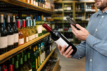 Man retail consumer scan electronic label of wine bottle with his smart phone in liquor store.