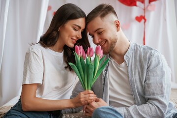 With beautiful flowers in hands. Young couple are together at home