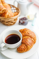 Baked tasty croissant and coffee cup on white table.