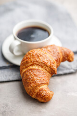 Baked tasty croissant and coffee cup on kitchen table.
