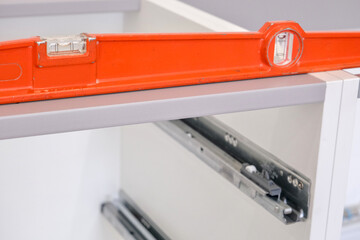 Orange level, placed on the structure of a kitchen base unit, to check its horizontality