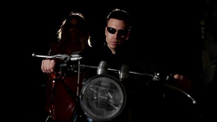 passionate blonde woman in shiny red dress approaching to cool man on motorbike, sexual people