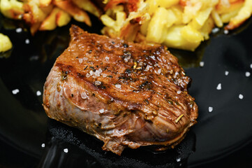 Roast beef steak with fried potatoes on a black plate. Close-up.