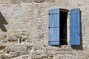 Fototapeta na wymiar Stone facade in Beaucaire, Provence, Gard, with blue shutters half closed.