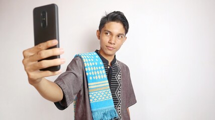 Asian Muslim man is holding and looking while smiling at a smartphone