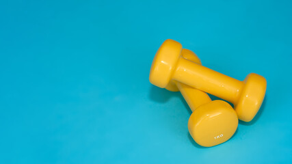 Sport. Yellow dumbbells on a blue background. Fitness. Training. Copyspace for text.