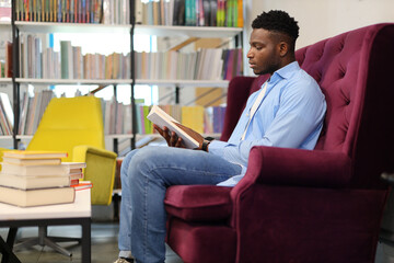 A young man sits in a library, surrounded by books, deeply engrossed in studying and contemplating...