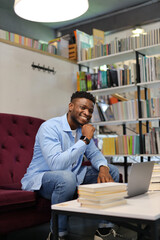 An African American young man sits confidently in a library, embodying intelligence and style as he studies and learns.