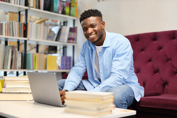 A diligent African American student in a university library, utilizing technology and books to...