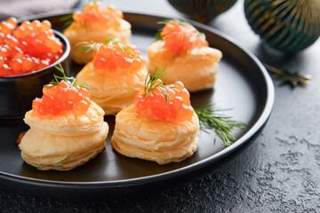 Salmon red caviar toast. Christmas canape or toast with red caviar on black plate on dark background. Idea to xmas snack. Gourmet food. Texture of caviar. Seafood.
