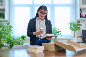 Woman with smartphone unpacking box with books, online shopping