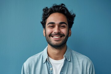 Obraz premium Smiling confident young adult arab man standing isolated on blue background. Happy ethnic guy student or professional employee wearing shirt looking at camera posing, Generative AI