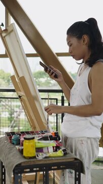 An Asian woman looks at her mobile phone next to her painting tools