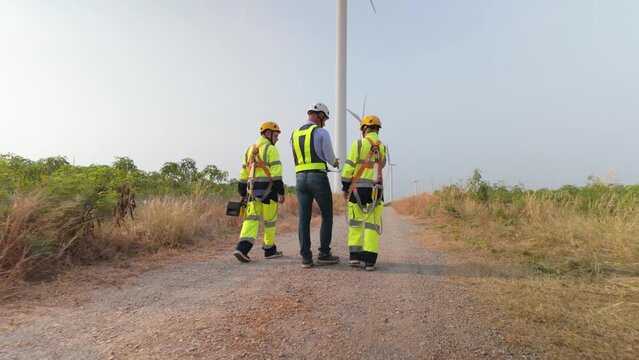 Engineers and inspector team wearing uniforms and helmets with equipment walking exploring and repairing electric wind turbines which are renewable energy for communities and agriculture. 4k video