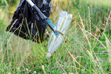 A volunteer picking up a discarded plastic bottle into a black trash bag from grass.