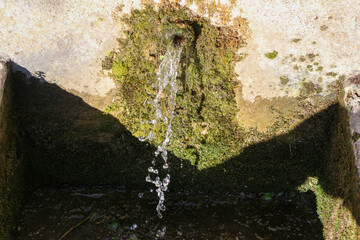 Close-up of a stone water fountain in a French village called Pélissanne, Pelissanne, Provence, South of France. Green moss, water running.
