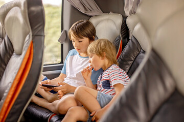 Children, siblings, playing on a mobile phone while traveling with bus on a long trip journey