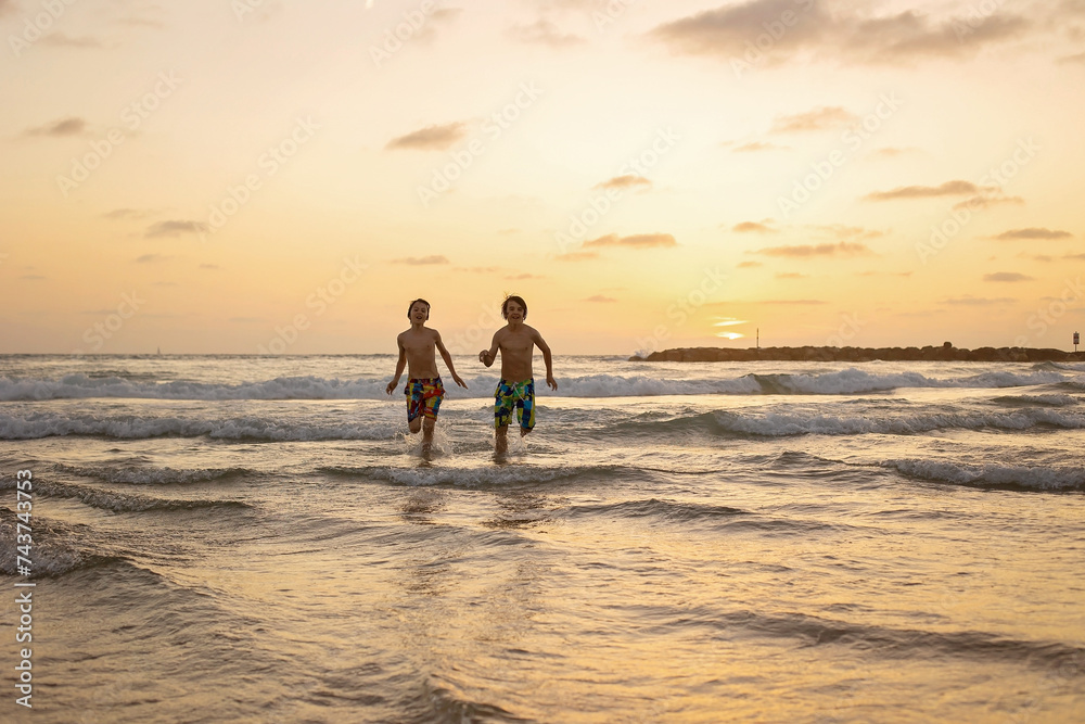 Canvas Prints Happy teenager boys, running and playing on the beach on sunset, splashing water and jumping on the sand