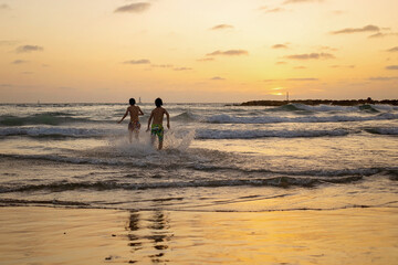 Happy teenager boys, running and playing on the beach on sunset, splashing water and jumping on the sand