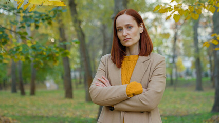 Serious offended Caucasian woman in autumn park in city outdoors posing confident alone looking at...