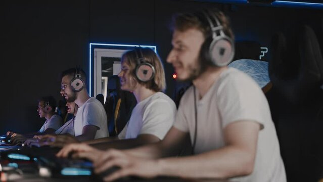 Team of gamers playing video game on PC at computer club, cyber sport. E-sport championship. 5 players in headset. Intense tournament, emotions. Multiplayer online, first-person shooter. Bristly guy
