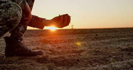 Farmer holding ground in hands closeup while sunset. Male hands touching soil on the field during...