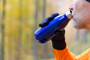 Male runner drining from vacuum flask at autumn forest backgroun