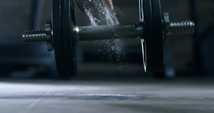 Super slow motion macro of male athlete hands with talc is doing workout by lifting weights of barbell to maintain healthy lifestyle and bodybuilding fitness goals in a gym at 1000 fps.