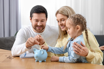Planning budget together. Little girl with her family putting coins into piggybank at table indoors
