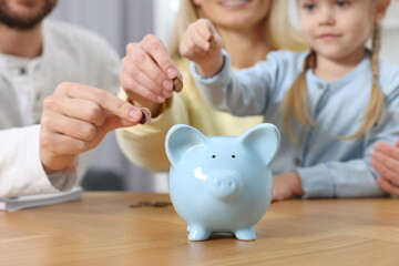 Planning budget together. Little girl with her family putting coins into piggybank at table, closeup