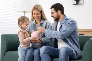 Planning budget together. Little girl with her parents putting coin into piggybank at home