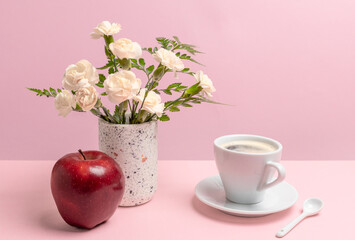 Bouquet of carnations in a vase with a an apple and a cup of coffee.