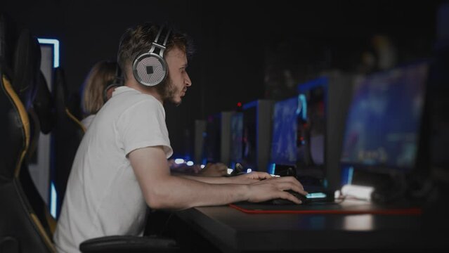 Bristly adult gamer in headset playing video game real-time strategy RTS at computer club with team, cyber sport tournament. E-sport championship. Player in headphones. Multiplayer online competition