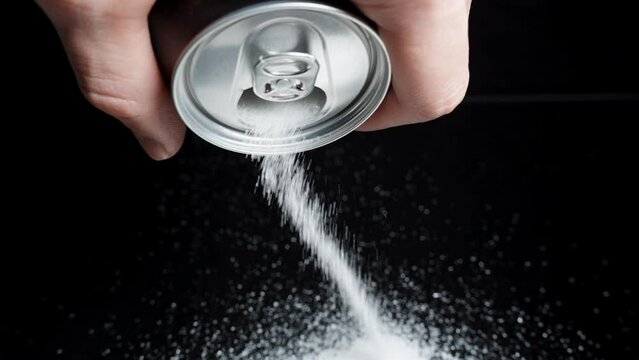 Pure white sugar being poured from a soda can onto a black table by a man. Concept of harmful drinks.
