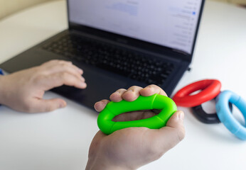 Hand gripper. Man squeezes rubber expander while working on his laptop. Concept of combining useful...